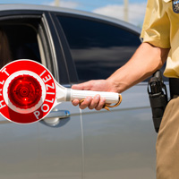 An der Seite eines silbernen Autos steht ein Polizist mit einer roten Halte-Kelle.